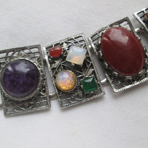 May include: A silver bracelet with a filigree design and colorful stones. The stones include purple, red, green, and white.