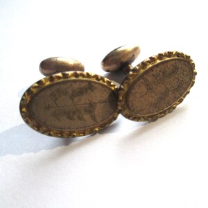 May include: A pair of gold oval cufflinks with a detailed design. The cufflinks have a textured edge and a raised design in the center.