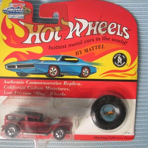 May include: Vintage Hot Wheels car packaging featuring a red and blue car with the text "Hot Wheels" in yellow and "hottest metal cars in the world! BY MATTEL" in white. The packaging also includes a red and blue car with the text "Authentic Commemorative Replica. California Custom Miniatures. Low-Friction "Mag" Wheels."