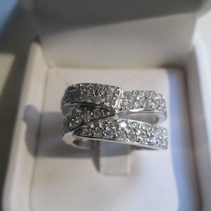 May include: A silver ring with two bands of pave set diamonds. The bands are intertwined and the ring is in a white box.