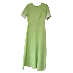 Könnte beinhalten: Hellgrünes Midikleid mit kurzen Ärmeln und strukturiertem Stoff. Das Kleid hat ein figurbetontes Oberteil und einen ausgestellten Rock. Die Ärmel sind mit weißer Spitze verziert. Das Kleid ist einfarbig und hat ein schlichtes, elegantes Design.