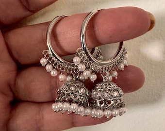 Puede incluir: Pendientes de aro plateados con colgantes en forma de campana. Los colgantes están adornados con pequeñas perlas blancas y detalles intrincados. Los pendientes están diseñados con una estética delicada y elegante, adecuados para ocasiones formales o informales.