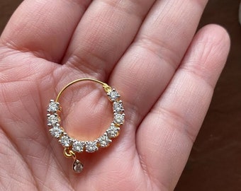 May include: A gold nose ring with a teardrop-shaped diamond dangle and a circle of small diamonds around the ring.