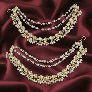 May include: A pair of gold-tone ear chains featuring multiple draped strands of small white beads. Each piece includes a metal hook for attachment, with circular settings holding white stones and dangling bead accents along the lower edge.