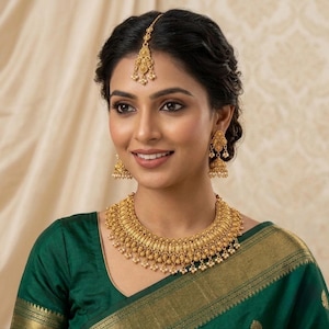 May include: A gold jewelry set consisting of a wide, ornate necklace with dangling beads, matching bell-shaped drop earrings, and a central forehead ornament. The pieces feature intricate metalwork and small white accents throughout the design.