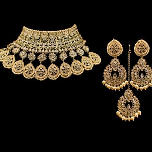 May include: A gold-tone bridal necklace and earrings set with pearl accents and clear stones. The necklace has a choker style with a teardrop design. The earrings are dangle style with a round design.