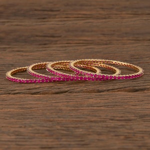 May include: Set of four gold bangles with pink gemstones. The bangles are stacked on top of each other.