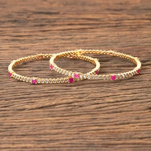 May include: Three gold bangles with a row of clear stones and pink square stones.