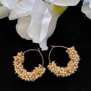 May include: A pair of gold hoop earrings with a cluster of small white pearls around the hoop.