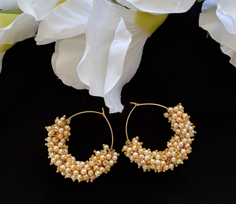 May include: A pair of gold hoop earrings with a cluster of small white pearls around the hoop.