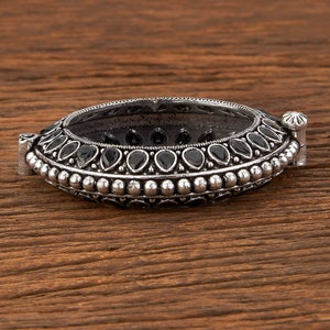 May include: A silver bangle bracelet with black stones set in a decorative design. The bracelet is open and has a hinged clasp.