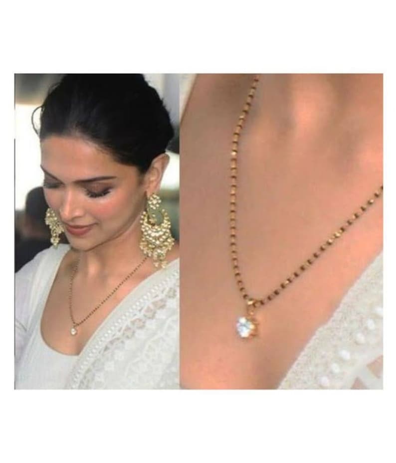 May include: A gold chain necklace with a small, clear stone pendant. The chain is black and gold and has a delicate design. The pendant is round and has a simple, elegant design.