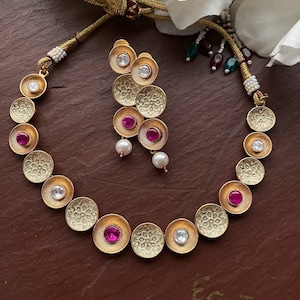 May include: A gold necklace with a series of round pendants, each with a white stone and a pink stone in the center. The necklace is paired with matching earrings.