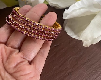 May include: Set of four gold bangles with purple glass beads. The bangles are stacked on top of each other.