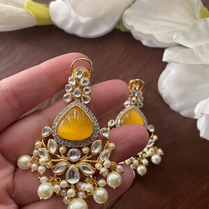 May include: A pair of gold earrings with a yellow teardrop-shaped stone and white pearl accents.