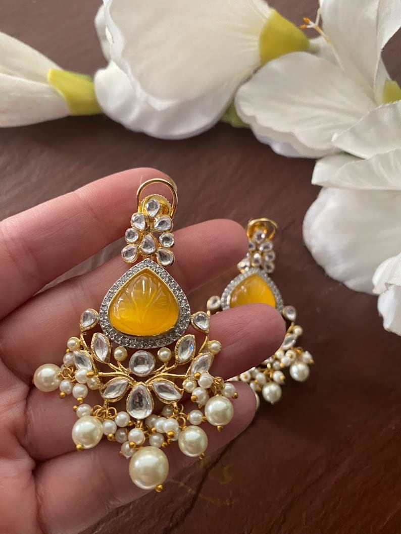 May include: A pair of gold earrings with a yellow teardrop-shaped stone and white pearl accents.