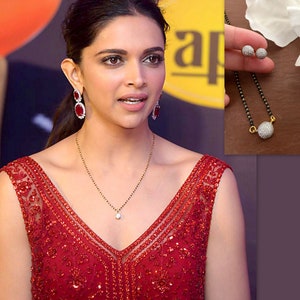 May include: A woman wearing a red sequined dress with a gold chain necklace and red gemstone earrings. The necklace has a small, round pendant with white stones. The image also shows a close-up of a black beaded necklace with a round pendant with white stones.