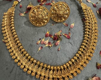 May include: A gold-toned necklace and matching circular stud earrings set. The necklace features a multi-layered design with repeating teardrop-shaped motifs and small spherical beads. The earrings mirror the intricate floral-like pattern.