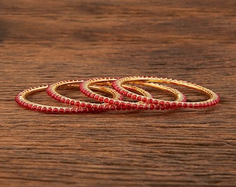May include: Set of four gold bangles with red bead accents. The bangles are stacked on top of each other.