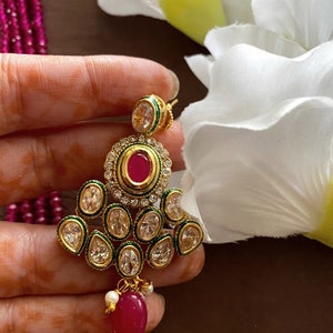 May include: Gold tone earrings with a pink stone and clear rhinestones. The earrings have a green trim and a dangling pink stone.