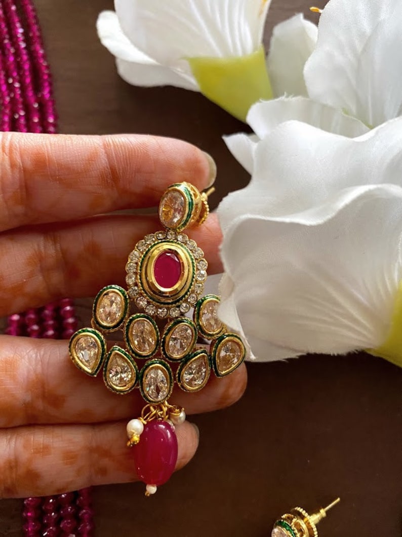 May include: Gold tone earrings with a pink stone and clear rhinestones. The earrings have a green trim and a dangling pink stone.