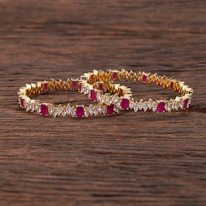 May include: Two gold bangles with a row of clear cubic zirconia stones and pink square stones.