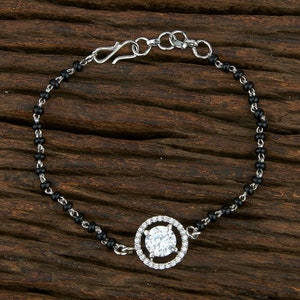 May include: A silver bracelet with a black bead chain and a round pendant featuring a large clear rhinestone surrounded by smaller rhinestones.