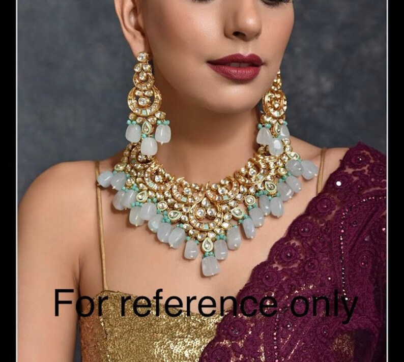 May include: A gold-toned necklace and earring set with clear and light blue accents. The jewelry features intricate detailing and a cascading design. The image includes the text "For reference only".
