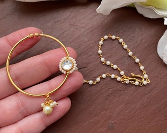 May include: Gold nose ring with a pearl chain and a round, clear stone set in a gold frame.