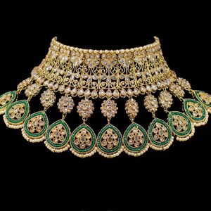 May include: A gold and green necklace with intricate detailing and a large pendant. The necklace is adorned with white stones and green beads.