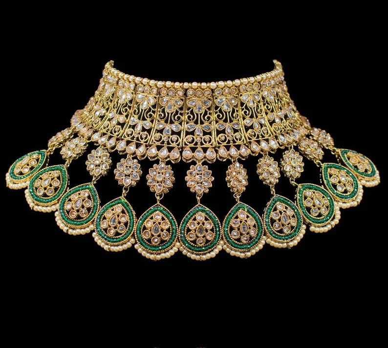 May include: A gold and green necklace with intricate detailing and a large pendant. The necklace is adorned with white stones and green beads.