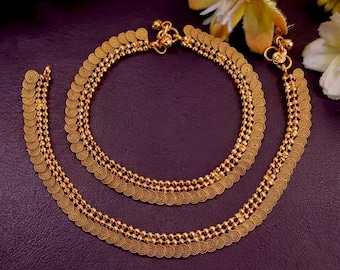 Könnte beinhalten: Ein Paar goldfarbene Metall-Fußkettchen mit einem mehrsträngigen Design, das komplexe kreisförmige Filigranmuster und kleine kugelförmige Perlen aufweist. Die Schmuckstücke sind durch einen Verschluss verbunden und haben ein metallisches Finish.