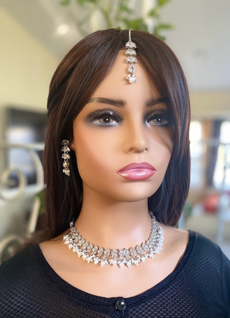 May include: A silver-toned necklace, earrings, and headpiece set. The jewelry features a leaf design with small white pearls. The necklace sits around the neck, the earrings dangle, and the headpiece is centered on the forehead.