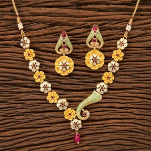 Peut inclure: Un collier doré et des boucles d'oreilles assorties. Le collier présente un motif floral avec des accents rouges et blancs. Les boucles d'oreilles ont une forme de goutte avec un pendentif floral. L'ensemble est présenté sur une surface en bois.