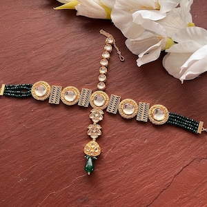 Może przedstawiać: Złota i zielona ozdoba do włosów z łańcuszkiem i wieloma okrągłymi, przezroczystymi kamieniami. Ozdoba ma zielony kamień w kształcie łzy na dole.