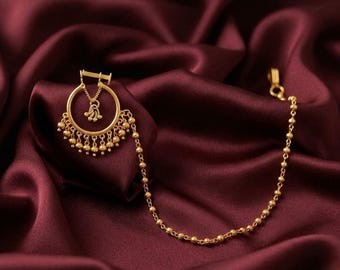 May include: A gold-toned nose ring featuring a circular hoop with a dangling central charm and a series of small spherical beads along the bottom edge. A long, delicate chain composed of small gold beads extends from the hoop to a clasp.