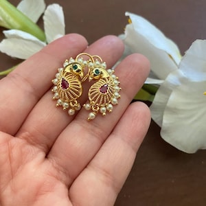 Pode incluir: Um par de brincos de ouro com um design de pavão. Os brincos são adornados com pequenas pérolas brancas e pedras preciosas vermelhas e verdes.