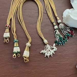 May include: Gold-colored beaded tassels with intricate designs. The tassels feature various bead colors, including white, green, and red, and are attached to gold cords. Each tassel has a small gold clasp.