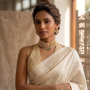 May include: A multi-strand pearl choker necklace featuring a central gold-toned pendant with a red stone and green accents, worn with a cream-colored halter-neck top with a subtle gold floral pattern and matching gold-toned drop earrings.