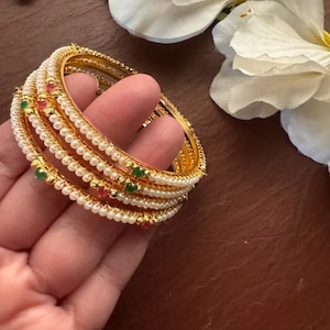 May include: Set of five gold bangles with pearl and green and red gemstone accents.