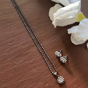 May include: A black chain necklace with a clear crystal pendant and matching earrings. The necklace and earrings have a delicate, floral design.