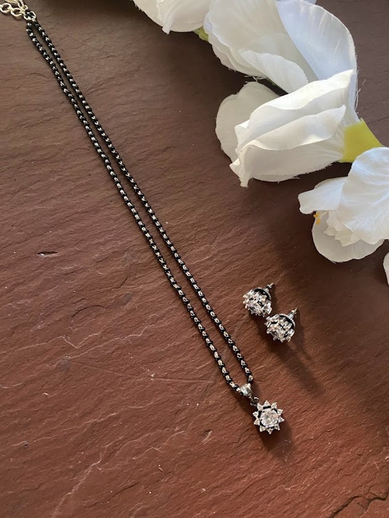 May include: A black chain necklace with a clear crystal pendant and matching earrings. The necklace and earrings have a delicate, floral design.