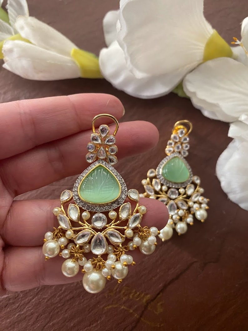 May include: A pair of gold earrings with a green stone and pearl accents. The earrings have a floral design and are dangling.