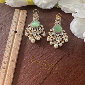 May include: A pair of green and gold dangle earrings with pearl accents. The earrings feature a carved green stone in the center of each earring.
