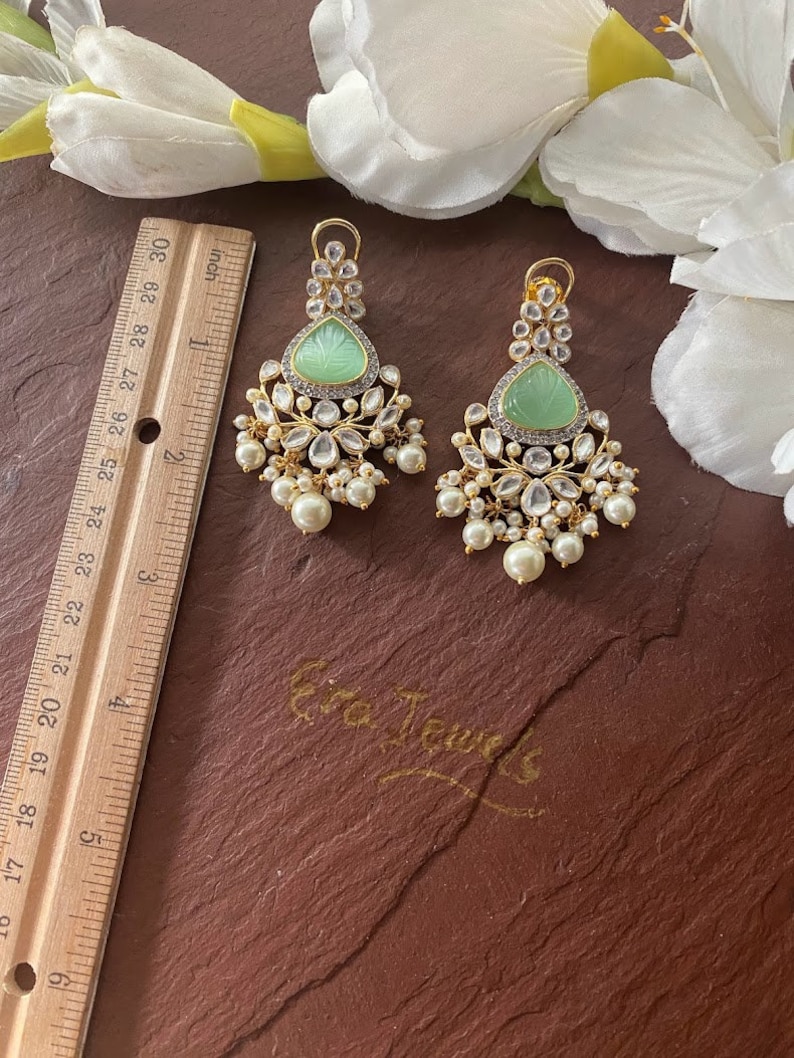 May include: A pair of green and gold dangle earrings with pearl accents. The earrings feature a carved green stone in the center of each earring.
