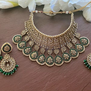 May include: A gold and green Indian bridal necklace set with a large, ornate choker, matching earrings, and a maang tikka. The necklace features intricate floral designs and is adorned with sparkling stones and pearls.