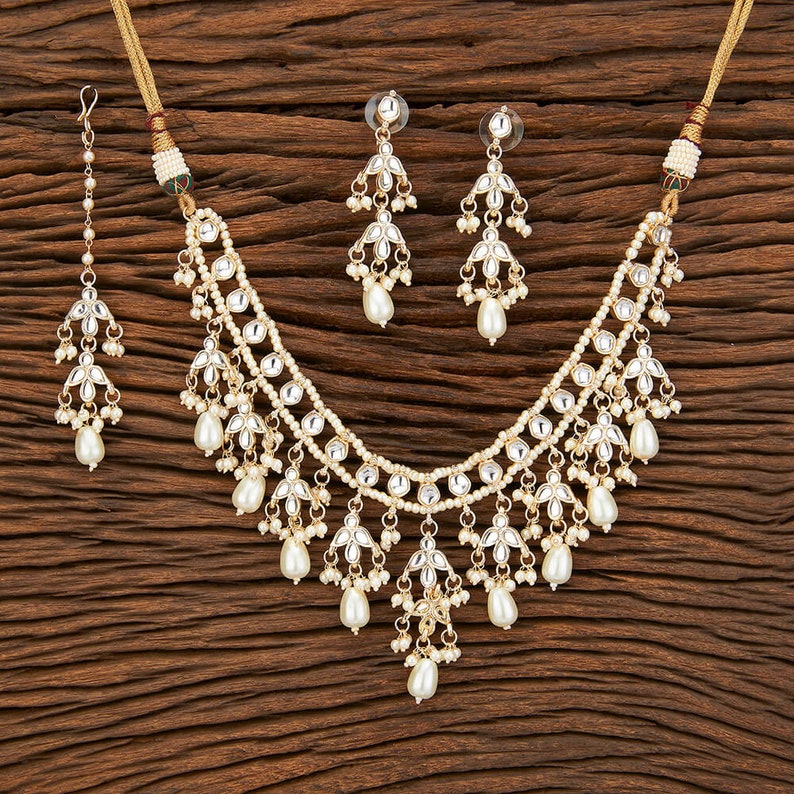 May include: A gold necklace with pearl and clear stone accents. The necklace has a layered design with multiple strands of pearls and stones. The necklace is paired with matching earrings.