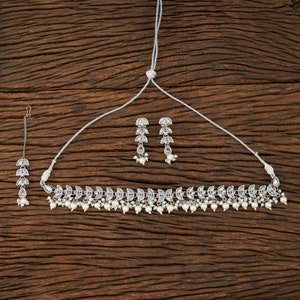 May include: A silver-toned jewelry set featuring a necklace, earrings, and a headpiece. The necklace and earrings have a leaf-like design with clear stones and small white pearls. The headpiece has a similar design.