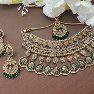 May include: A gold and green Indian bridal necklace set with intricate detailing and pearl accents. The set includes a choker necklace, earrings, and a maang tikka.
