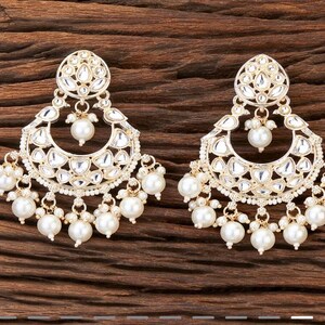 May include: A pair of gold-toned chandelier earrings with a floral design. The earrings feature a large, teardrop-shaped pearl at the bottom and smaller pearls dangling from the bottom. The earrings have a detailed, ornate design with clear, reflective accents.